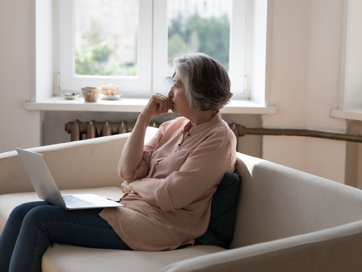 A woman sitting on a couch with a laptop, considering when to see a retina specialist